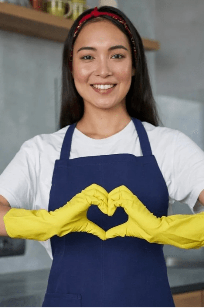 A smiling cleaning professional forming a heart with yellow-gloved hands